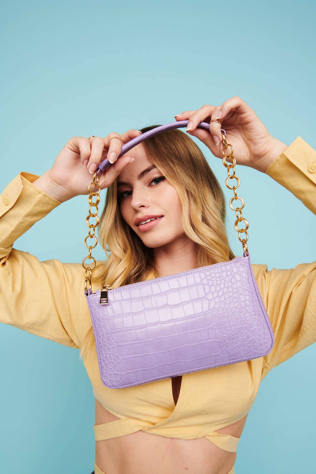 A girl in a yellow top holding a purple purse in front of a blue background	
