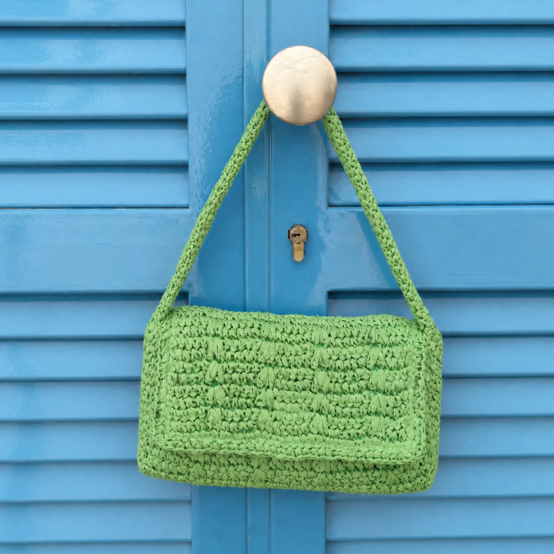 Green crocheted handbag hanging on a blue door with a brass doorknob.
