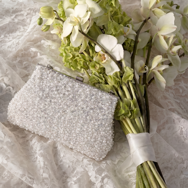 Pearl clutch bag on a lace surface with a bouquet of flowers
